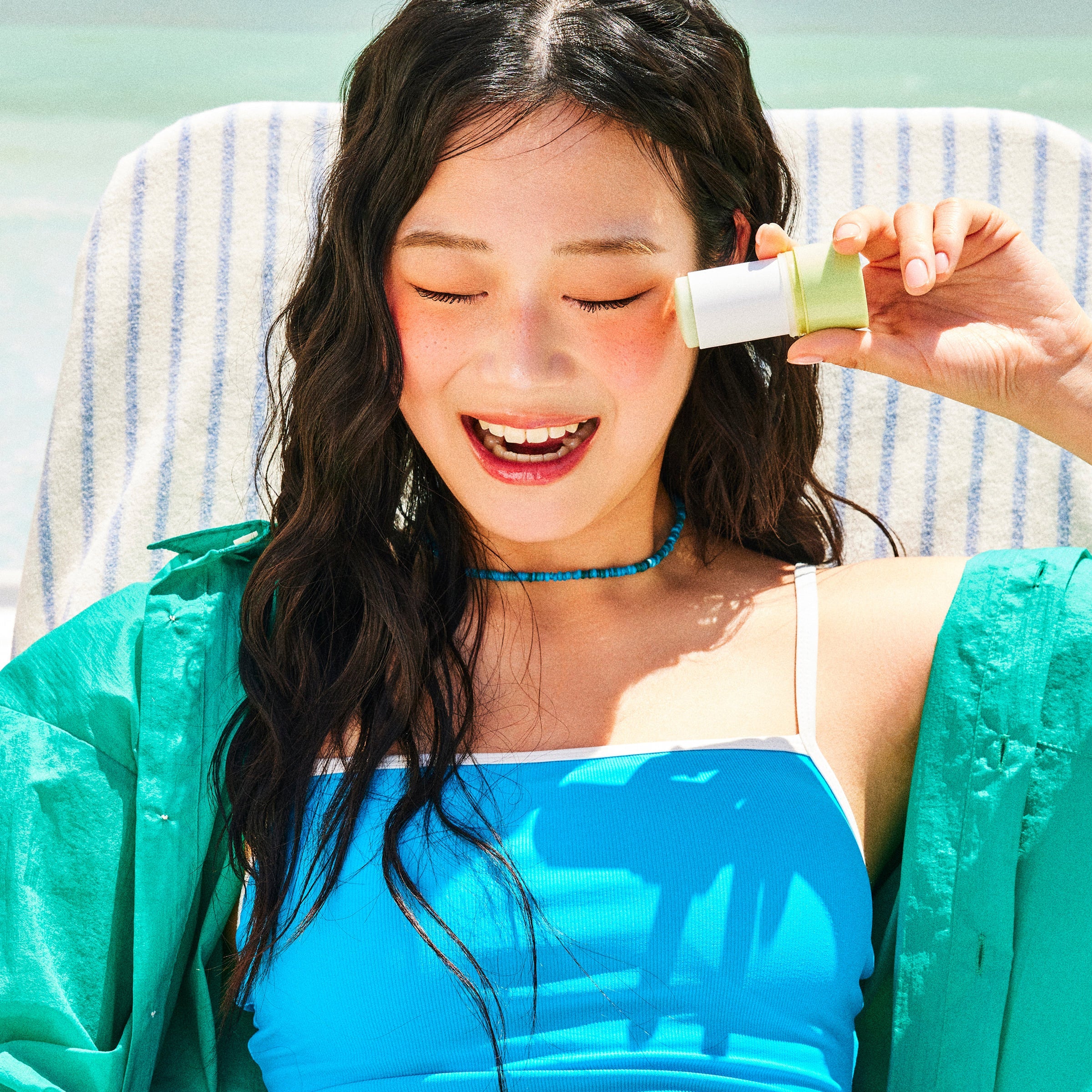 Person holding LADOR Tamanu Oil Sun Stick 21g, enjoying sunshine on a striped chair.