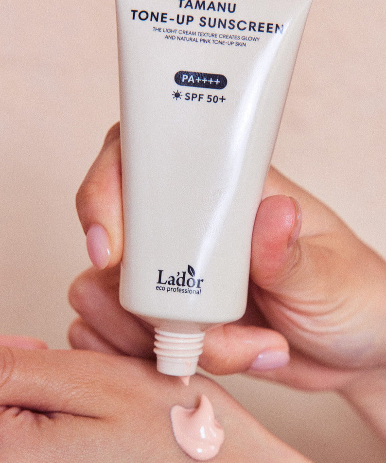 Person applying LADOR Tamanu Tone Up Sunscreen 50ml on hand, SPF 50+, PA++++ protection, tube, light cream texture for glowy tone-up skin.