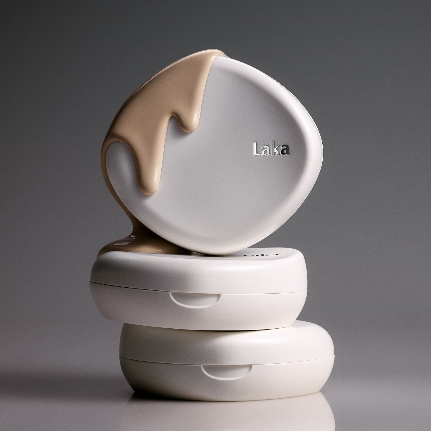 Stack of LAKA Bonding Cover Cushion compacts with beige cream flowing over the top, highlighting the LAKA Bonding Cover Cushion product.