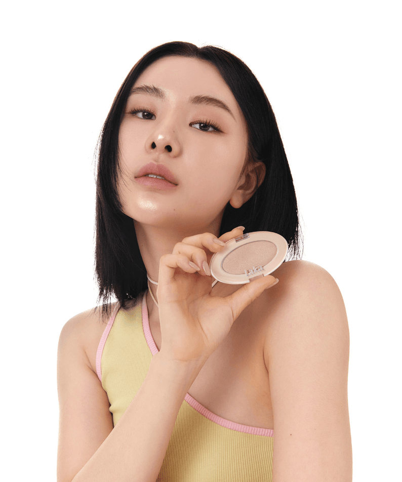 Woman holding LAKA DreamBeam Higlighter in a yellow top, showcasing the product's packaging.