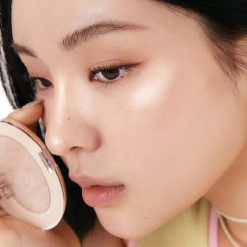 Woman applying LAKA DreamBeam Higlighter for a radiant glow on her cheek.