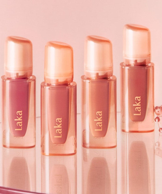 Four bottles of LAKA Jelling Nude Gloss displayed on a reflective surface with a pink backdrop.