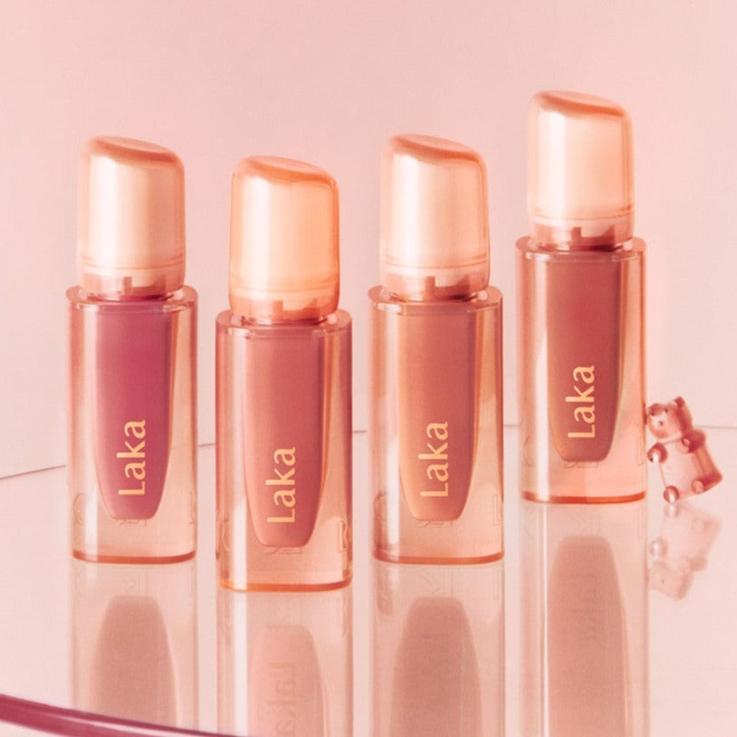 Four bottles of LAKA Jelling Nude Gloss displayed on a reflective surface with a pink backdrop.