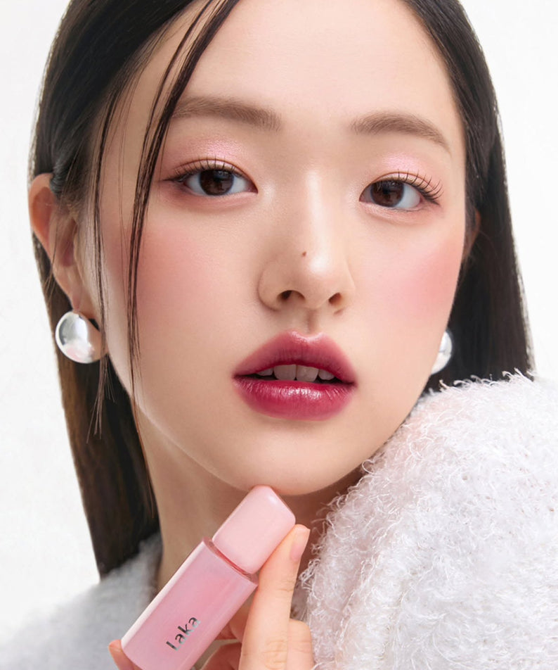 Person holding LAKA Popping Balloon Tint with pink lipstick, showcasing beauty and makeup application.