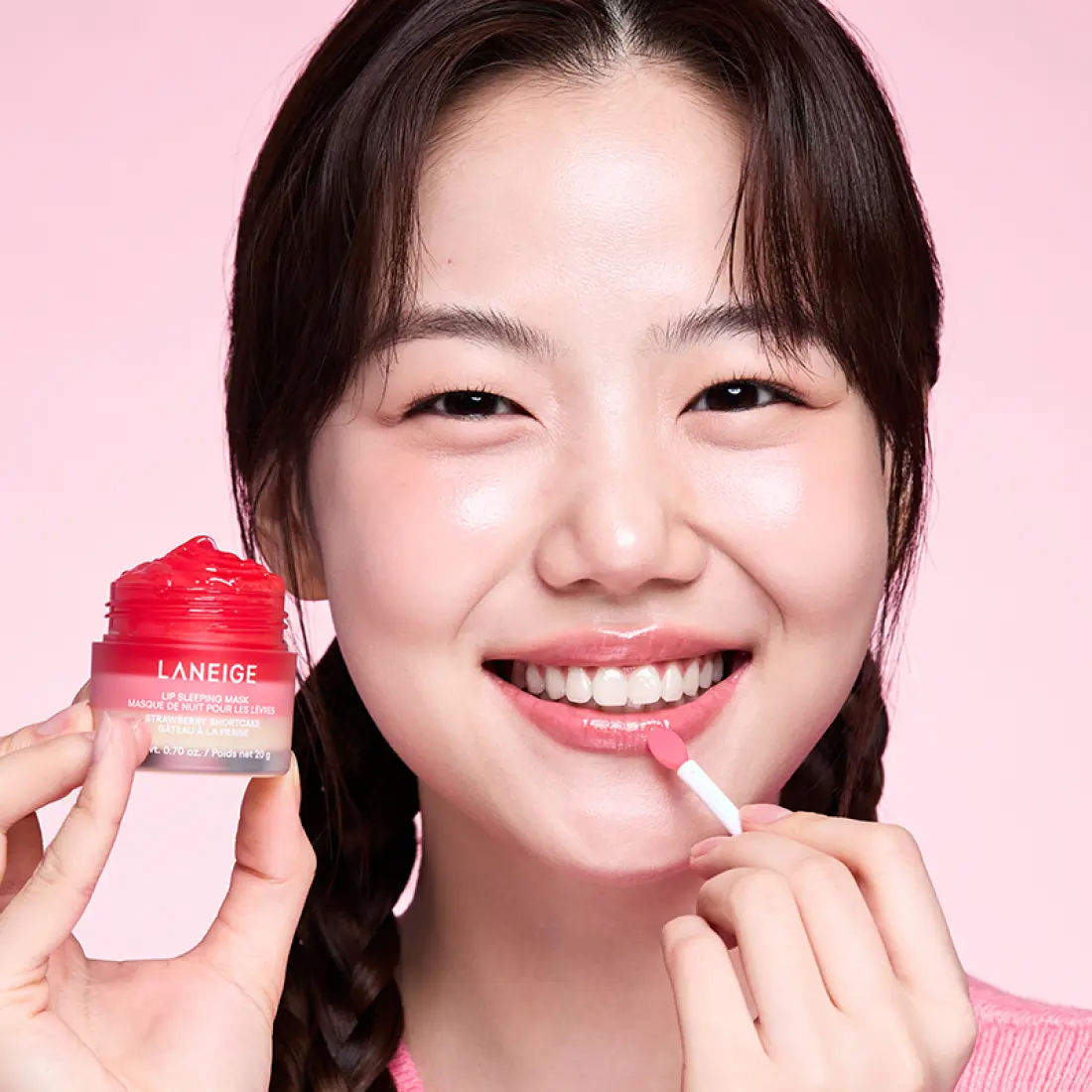 Woman applying LANEIGE Lip Sleeping Mask EX Strawberry Shortcake 20g with smiling expression and pink background.