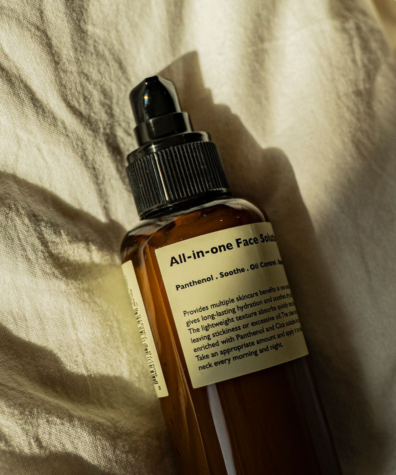 Gentleman Korea product shot of LAZY SOCIETY All-in-One Face Solution 150g bottle for men skincare, brown pump bottle on fabric, premium Korean grooming
