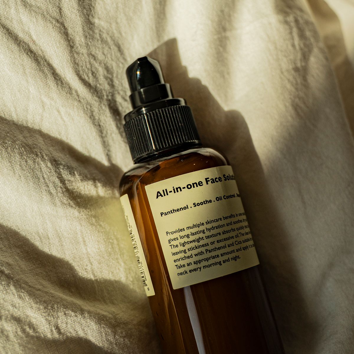 Gentleman Korea product shot of LAZY SOCIETY All-in-One Face Solution 150g bottle for men skincare, brown pump bottle on fabric, premium Korean grooming
