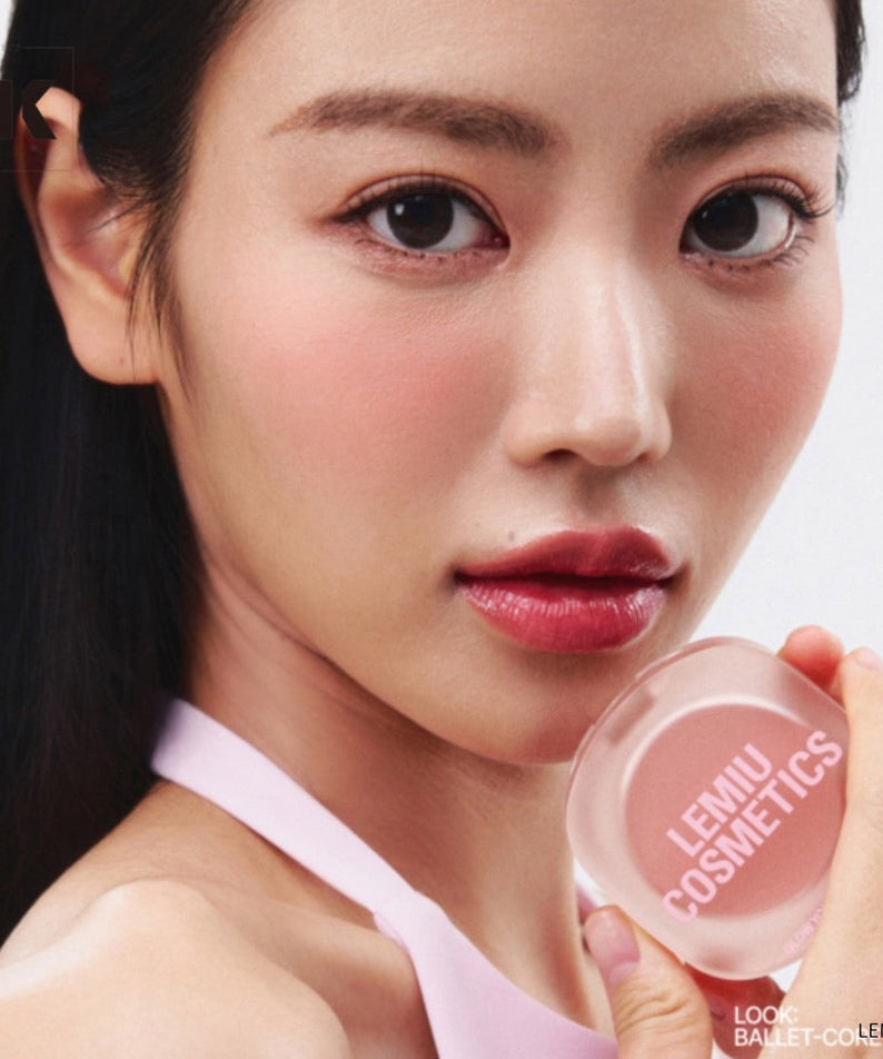 Woman holding LEMIU Eye To Cheek cosmetic product in hand, showcasing its vibrant pink color and texture for makeup application.