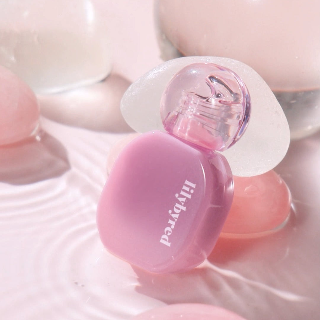 LILYBYRED Balming Dewy Tint in a pink hue with a stylish transparent cap placed on a reflective surface.