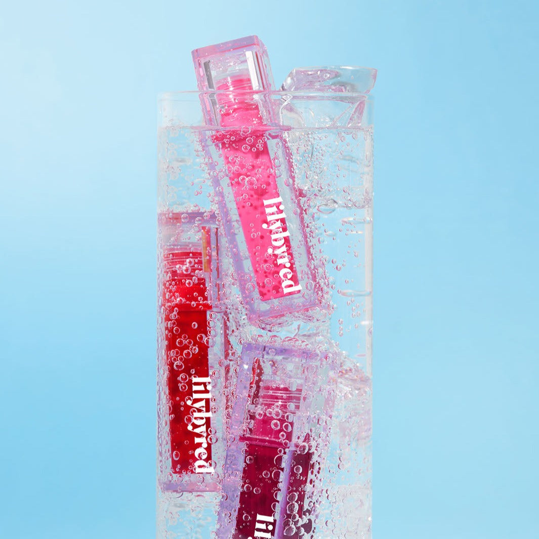 LILYBYRED Juicy Liar Water Tint bottles submerged in a glass of sparkling water against a blue background.