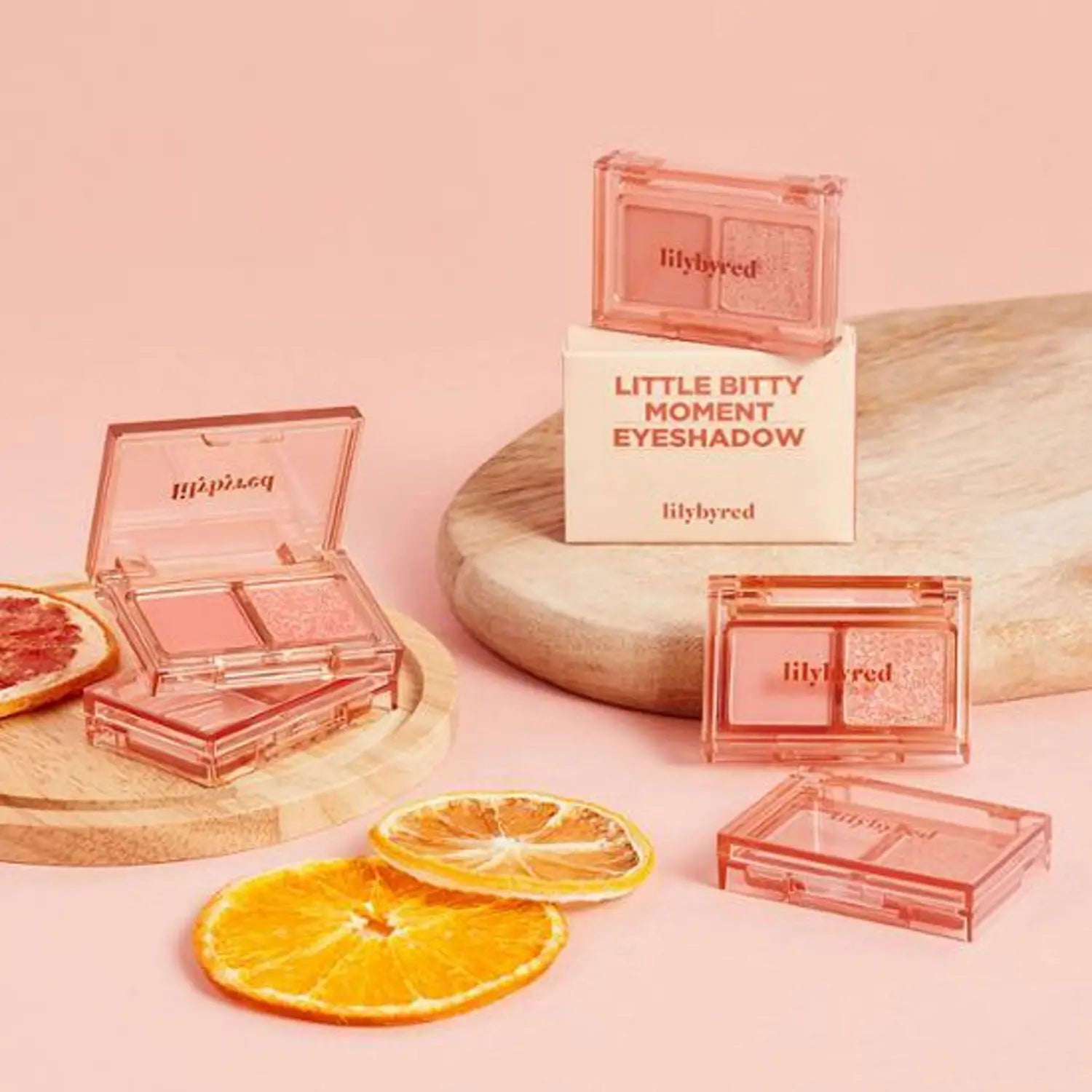 LILYBYRED Little Bitty Moment Shadow in pink packaging on a wooden tray with citrus slices, enhancing any makeup collection.