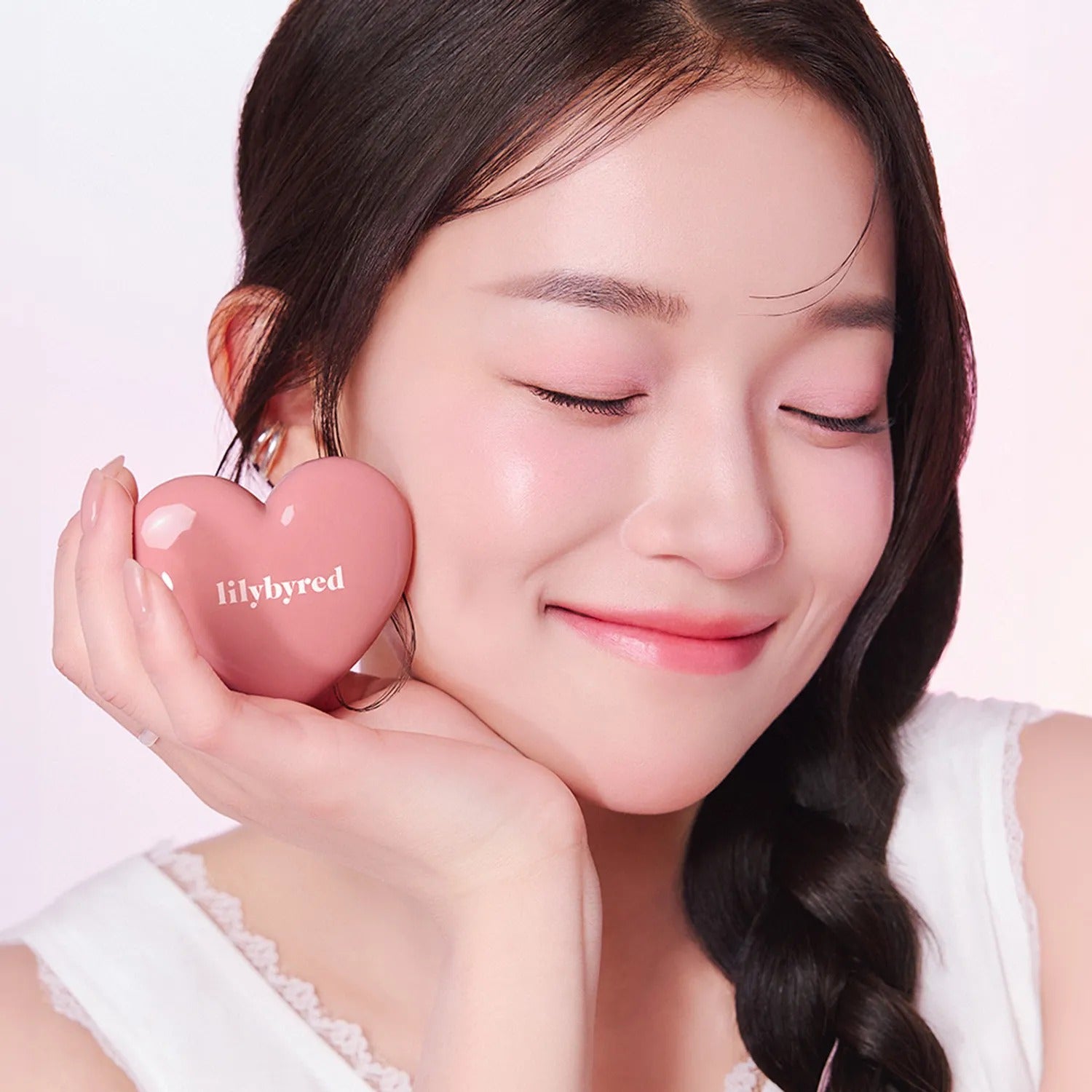 Woman holding LILYBYRED Love Beam Cheek Balm in heart-shaped container, showing natural glow and blush.