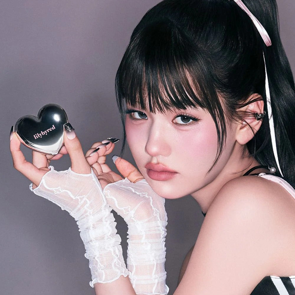 Model holding heart-shaped LILYBYRED Love Beam Cheek Mousse, showing blush effect on cheeks.