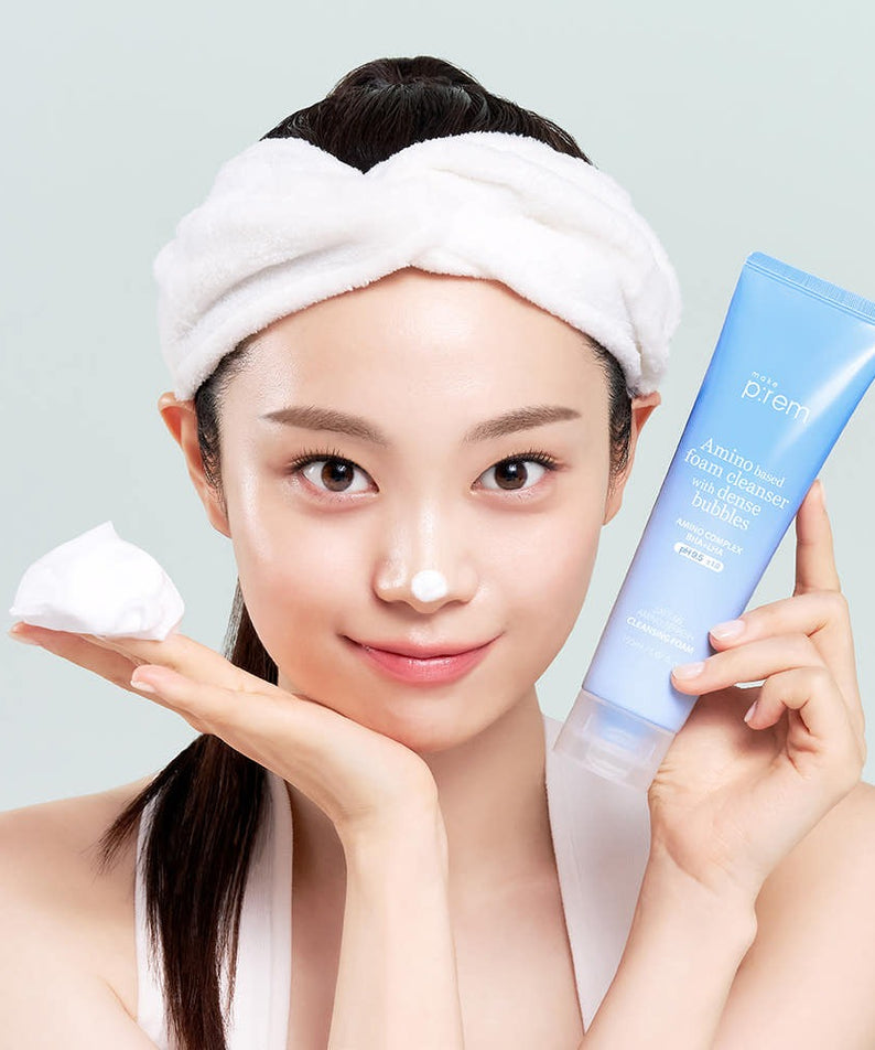 Person holding MAKE P:REM Safe Me Amino Refresh Cleansing Foam 150ml beside face, with cleansing foam on nose and headband on.