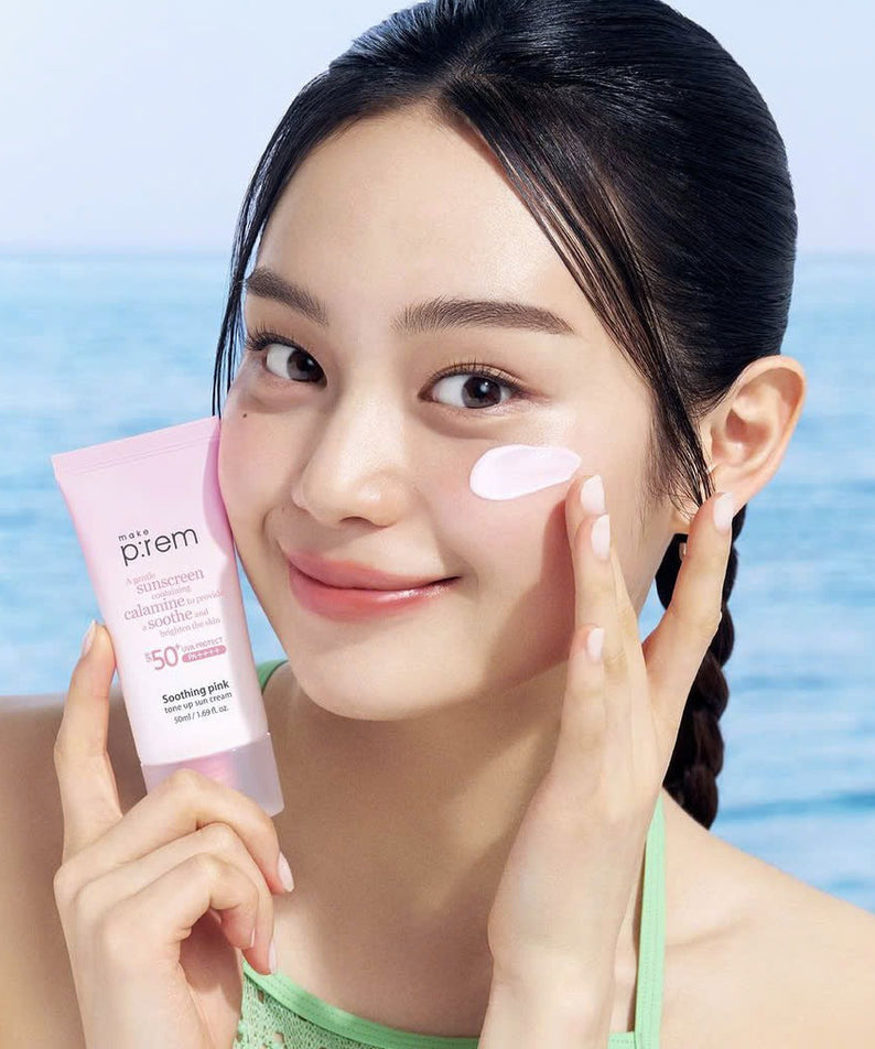 Woman applying MAKE P:REM Soothing Pink Tone-Up Sunscreen SPF 50+ PA++++ 50ml near ocean