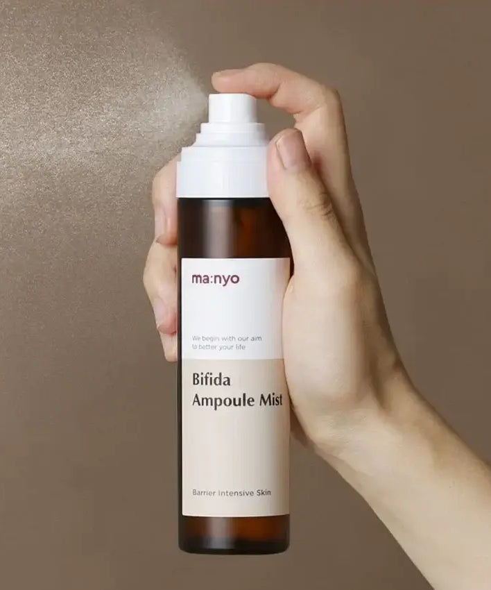 Person holding MANYO Bifida Ampoule Mist 120ml spray bottle against a brown background