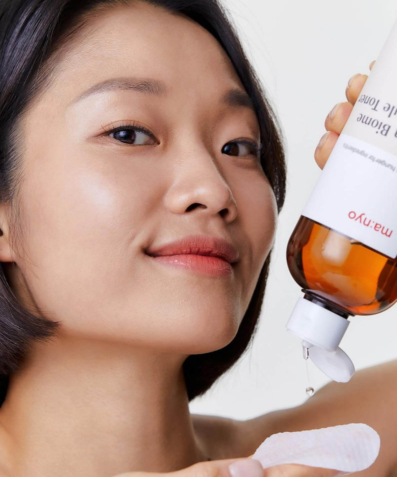 Woman applying MANYO Bifida Biome Ampoule Toner 400ml to cotton pad, showcasing skincare routine.