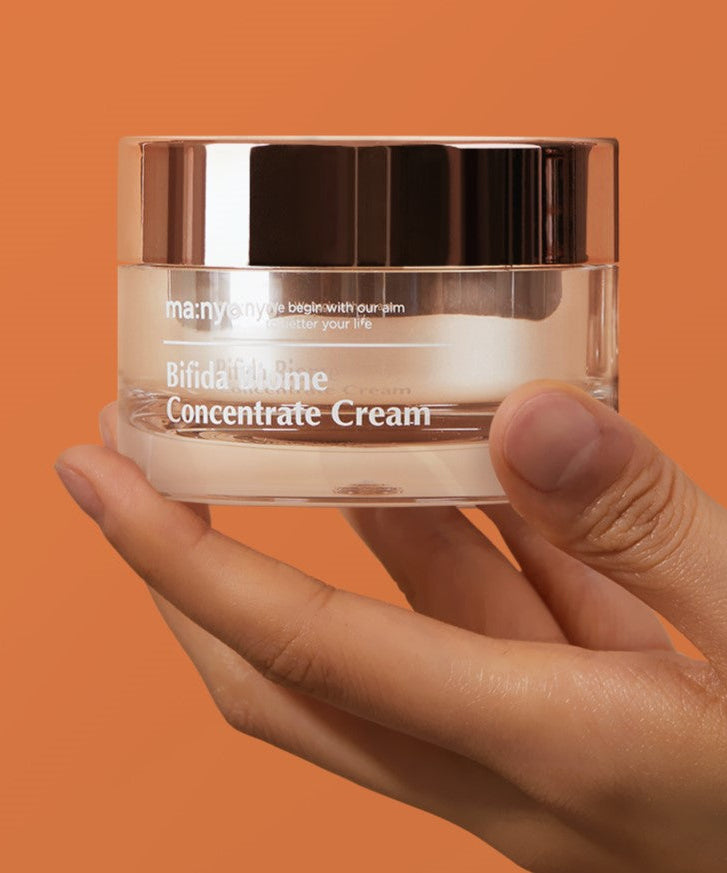 MA:NYO Bifida Biome Concentrate Cream 50ml in hand, showcasing the product packaging against an orange background.