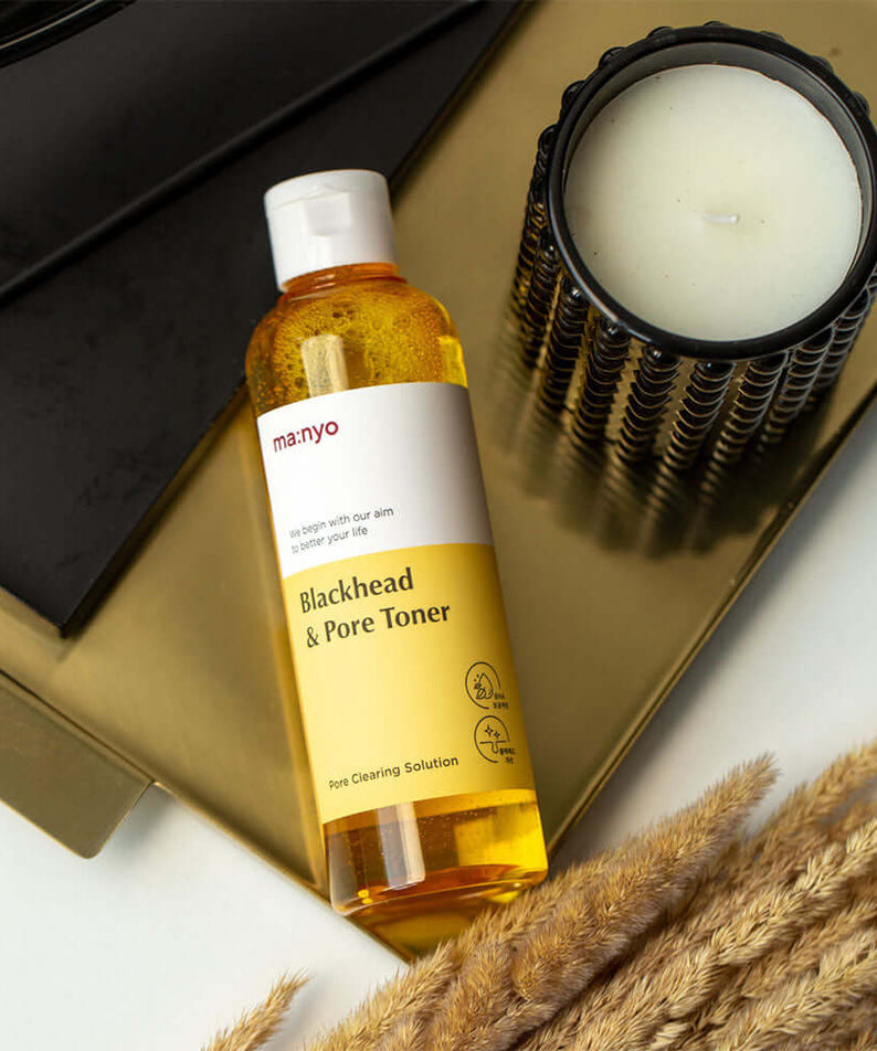 MANYO Blackhead & Pore Toner 210ml bottle on a gold tray next to a candle, featuring skincare benefits for blackheads and pores.