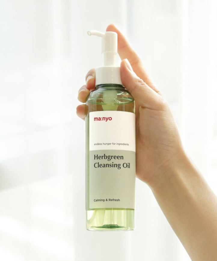 Hand holding MA:NYO Herbgreen Cleansing Oil 200ml bottle against a light background.