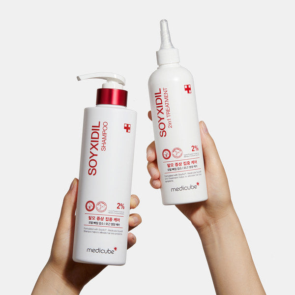 Hands holding MEDICUBE Soyxidil 2 Set (Treatment 265ml, Shampoo 490ml) showing product labels and design.