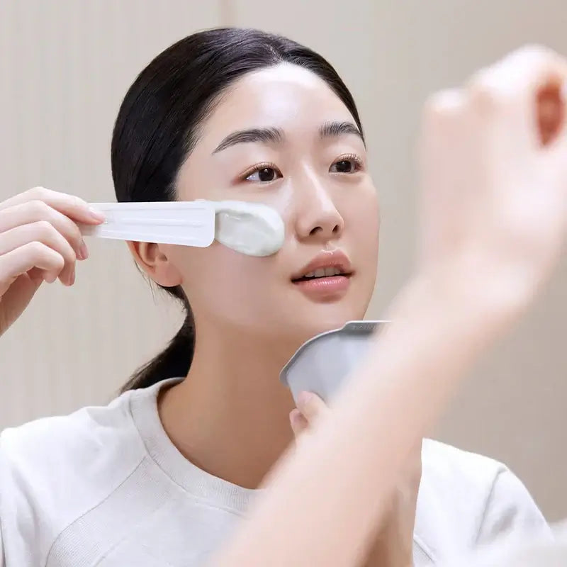 Woman applying MEDIHEAL Derma Modeling Pack [Hyaluronic Acid Moisturizing] to her face with a spatula