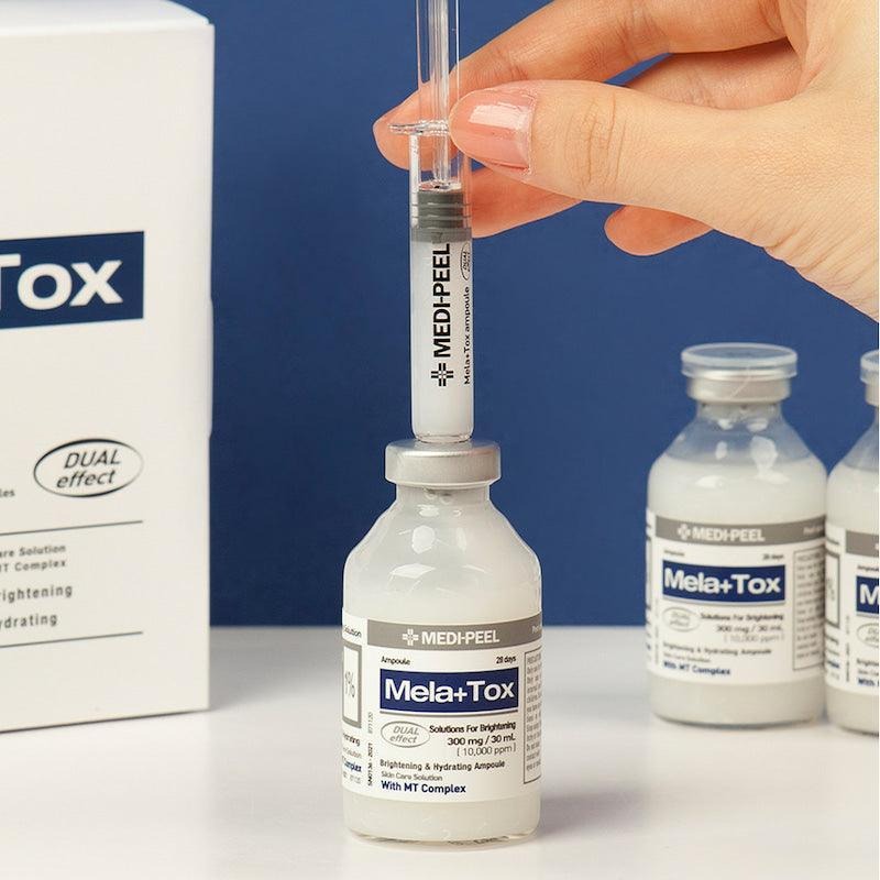 Hand holding syringe above MEDIPEEL Mela Plus Tox Ampoule 35ml with product displayed on table