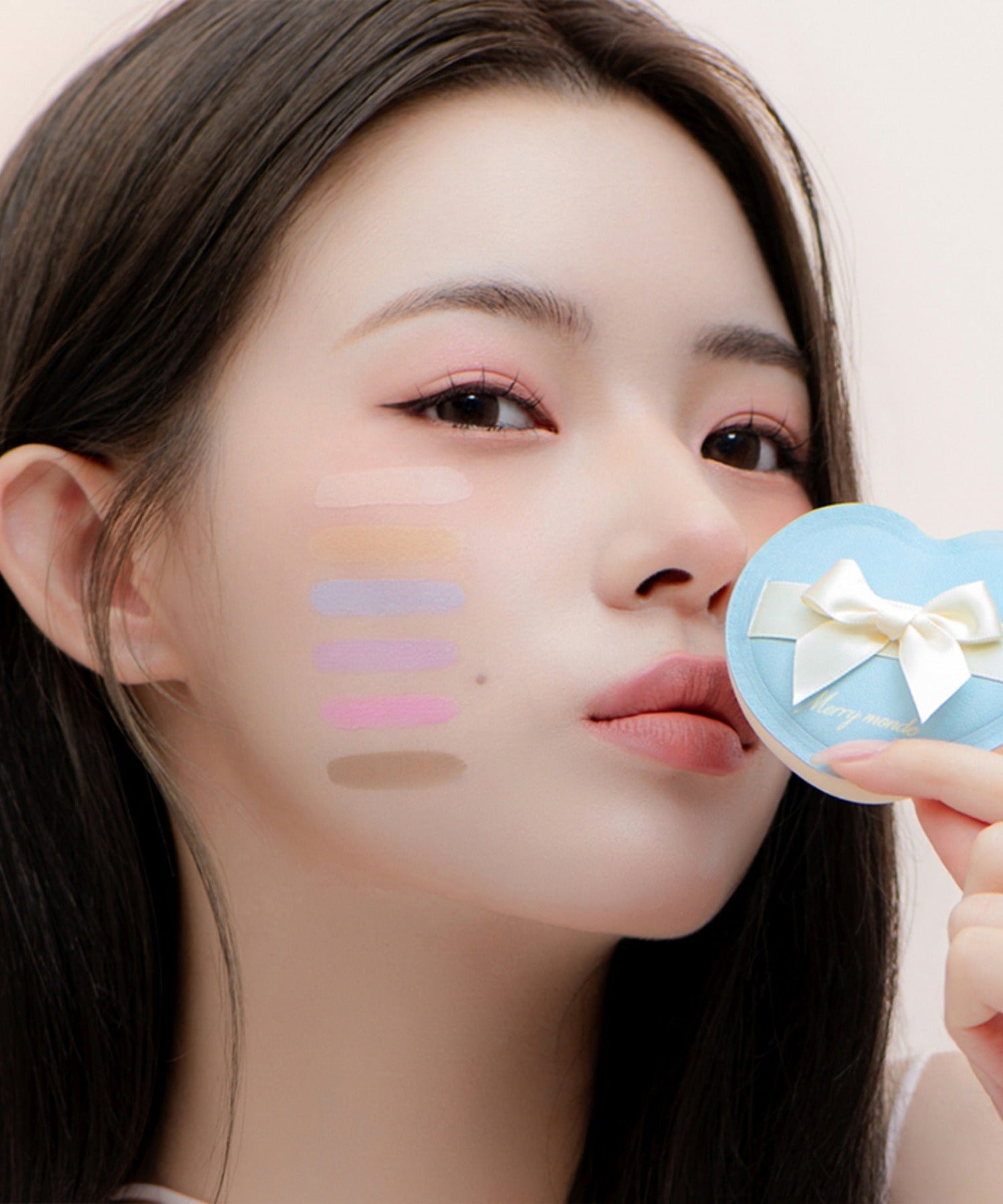 Woman holding MERRY MONDE Merry Everyday Color Correcting Concealer with swatches on cheek