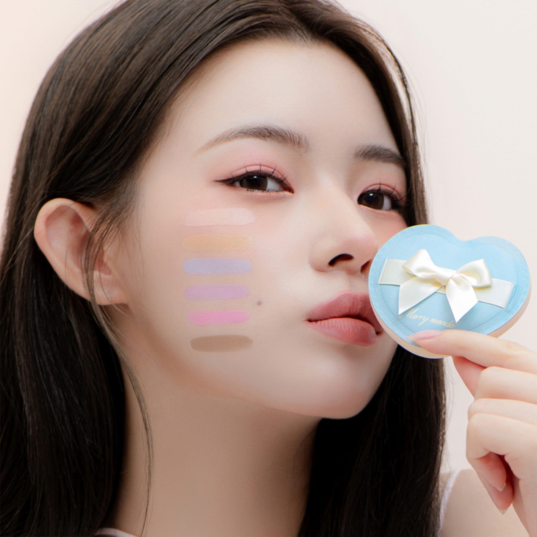 Woman holding MERRY MONDE Merry Everyday Color Correcting Concealer with swatches on cheek