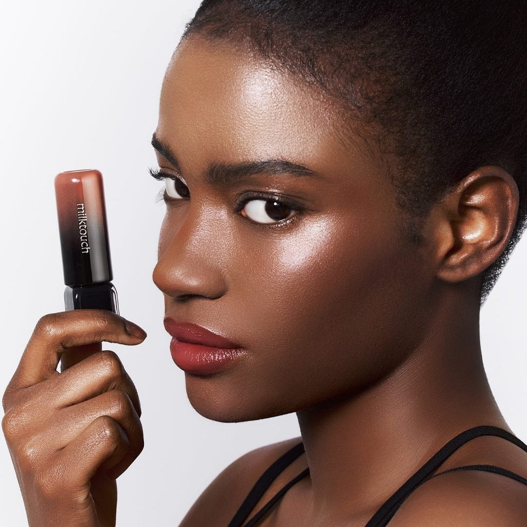 Model showcasing MILK TOUCH Black Peel-Off Lip Tattoo in hand, highlighting its vibrant color and peel-off application.