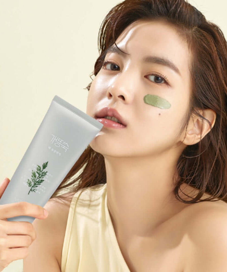 Woman holding MISSHA Artemisia Pack Foam Cleanser 150ml with green dab on cheek