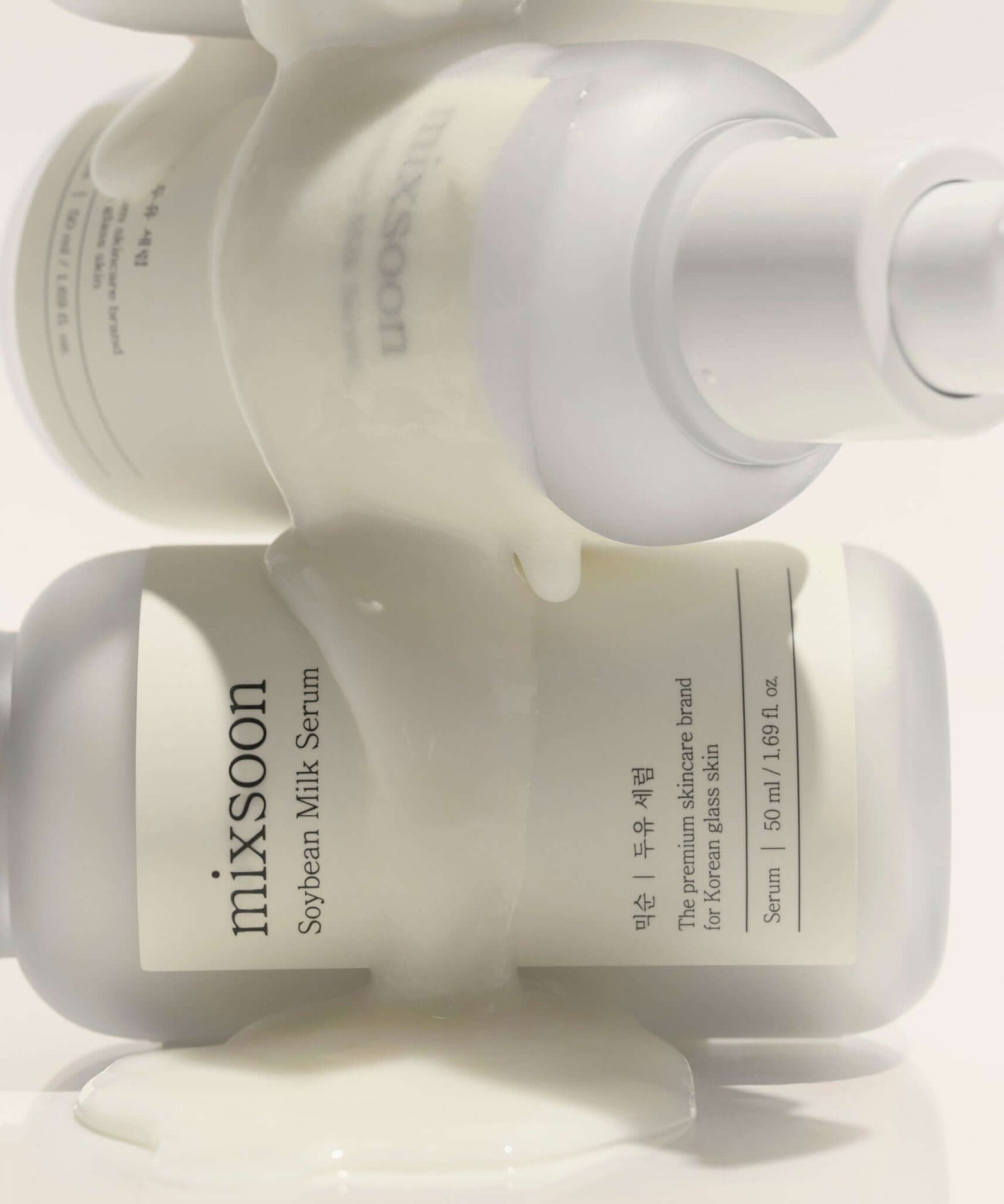 MIXSOON Soybean Milk Serum 50ml bottles with white liquid flowing over them, showcasing skincare product design and packaging.