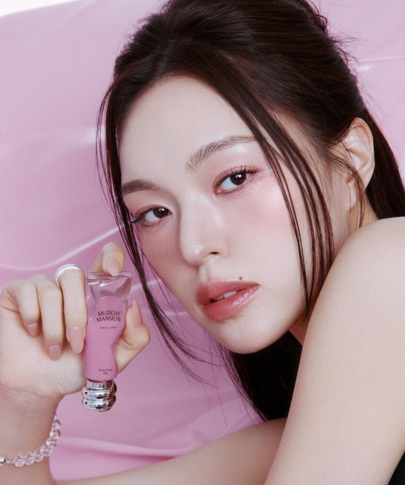 Person holding MUZIGAE MANSION Object Glossy tube with a pink background, showcasing beauty product.
