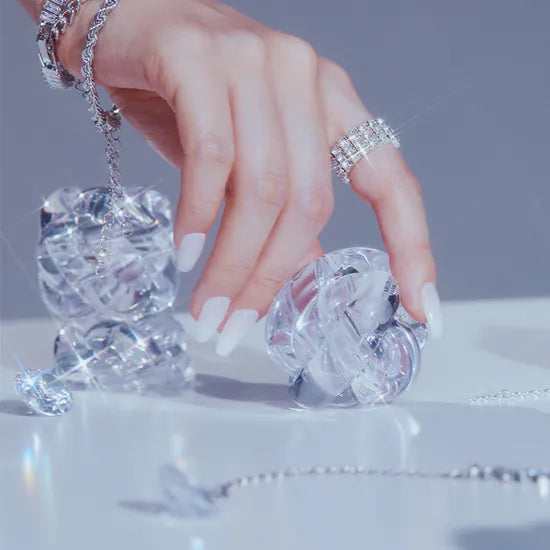 Hand adorned with jewelry holding crystal ornaments against a soft background.