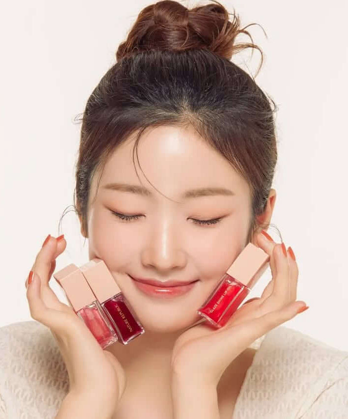 Woman smiling holding NATURE REPUBLIC Glaze Shine Lip Oil bottles