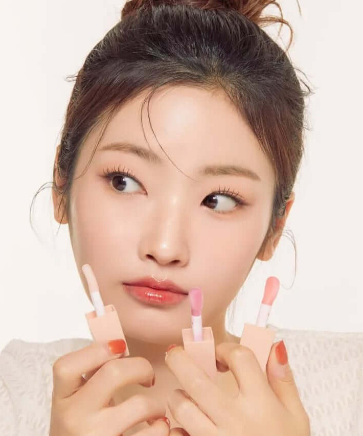 Woman holding NATURE REPUBLIC Glaze Shine Lip Oil with various shades, showcasing shiny lip finish.