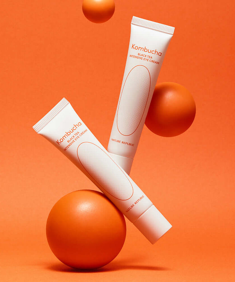 NATURE REPUBLIC Kombucha Black Tea Eye Cream 30ml tubes on an orange background with orange spheres.