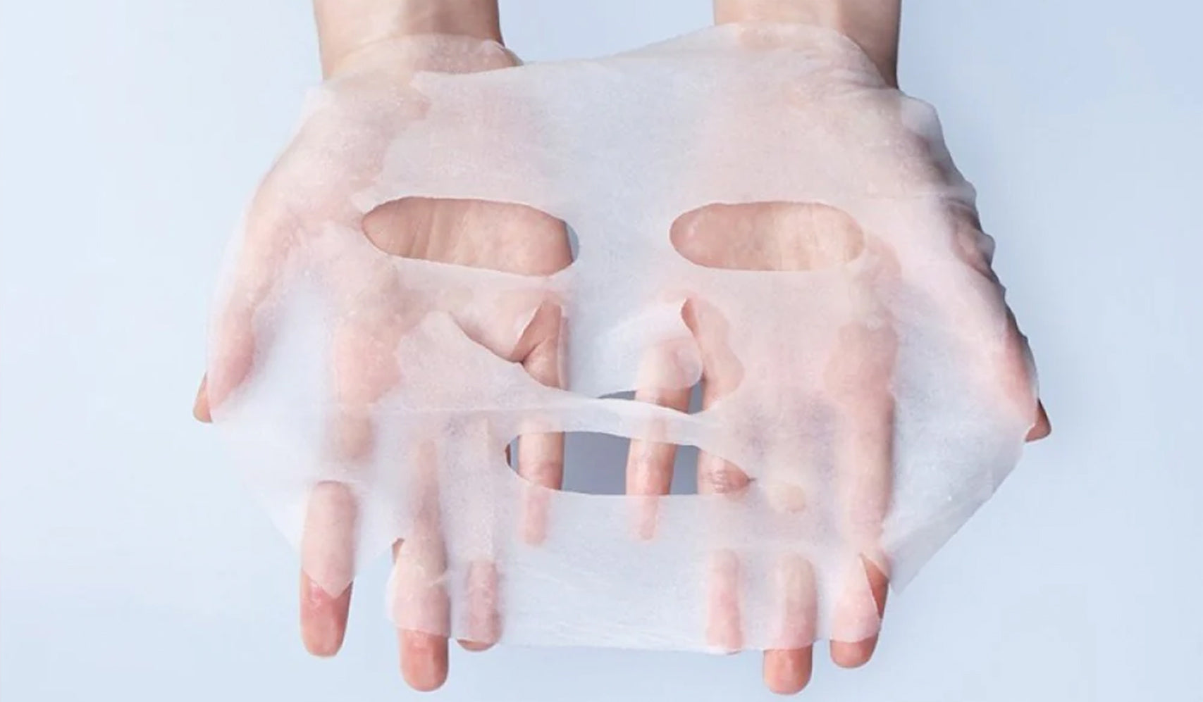 Hands holding a white sheet mask for skincare routine