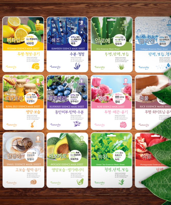 NATUREBY Essence Mask Pack 1+1 variety on wooden table with green leaves, including vitamin, seaweed, avocado, and more skincare masks