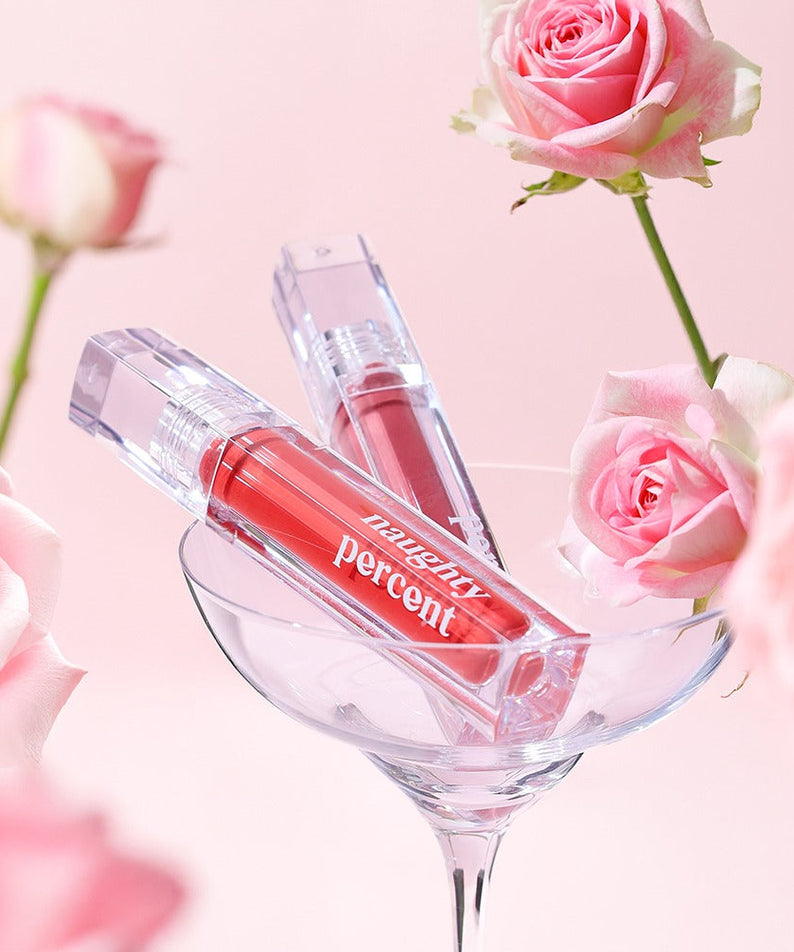 NAUGHTY PERCENT Matte Bloom Tint product displayed with pink roses in a glass, showcasing vibrant color and elegant packaging.