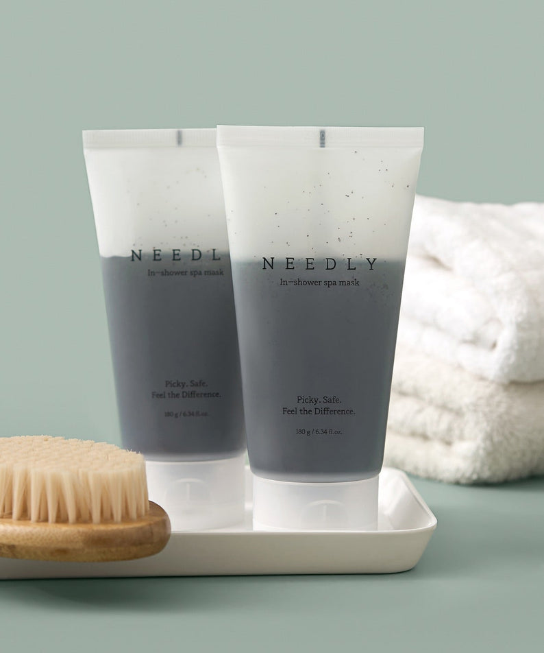 Two tubes of NEEDLY Ishower Spa Mask 180g next to a dry brush and towels, highlighting spa-like skincare experience.
