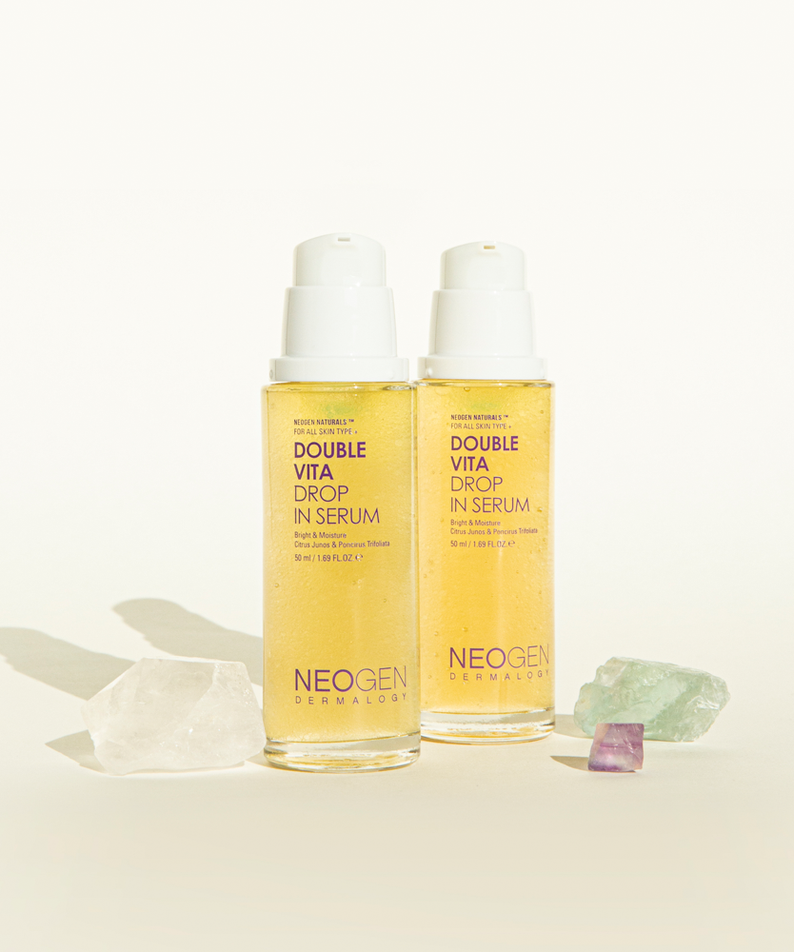 Two bottles of NEOGEN Double Vita Drop in Serum 50ml with gemstones, showcasing skincare product.