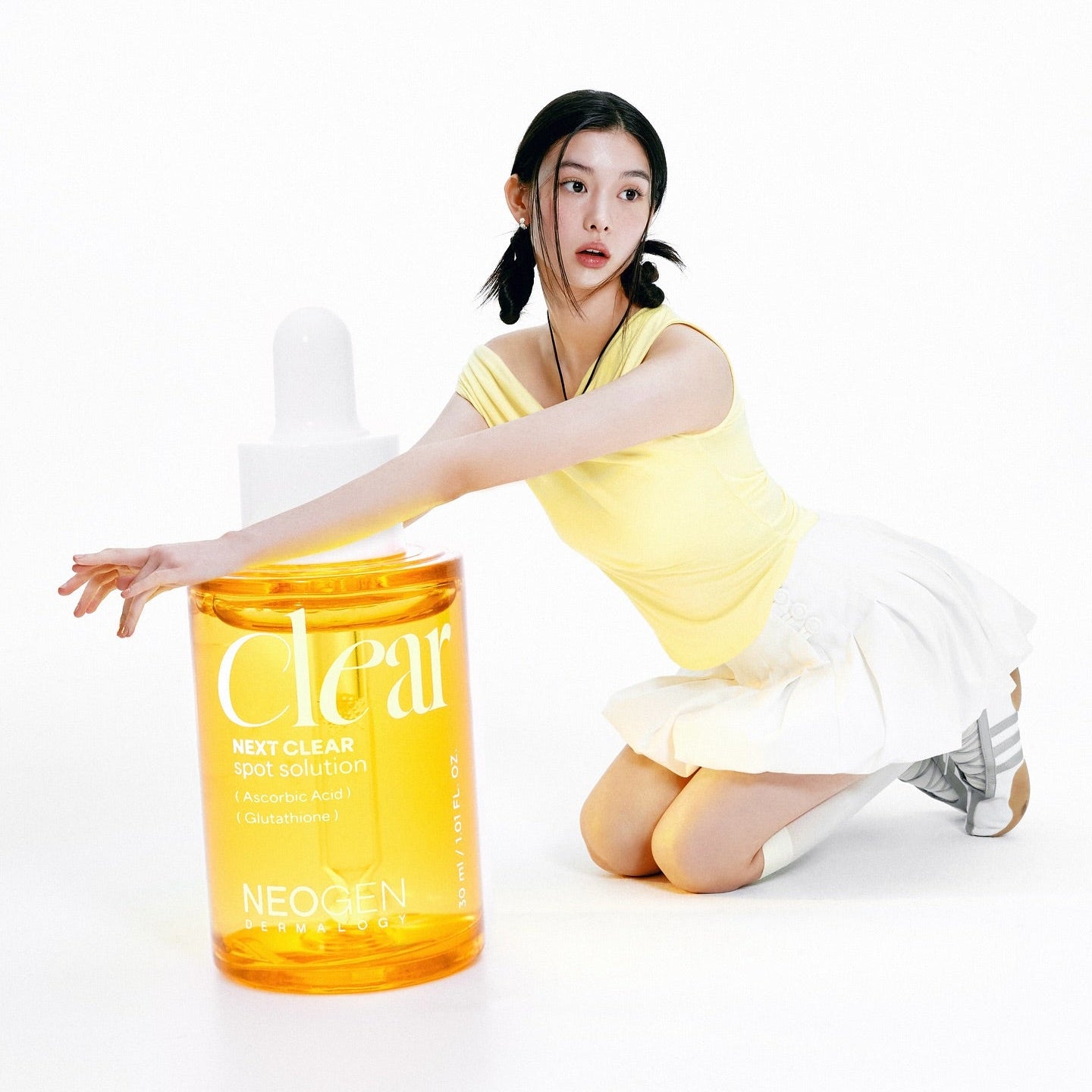 NEOGEN Next Clear Spot Solution 32ml bottle with a person in a yellow top, illustrating the product's size and design.