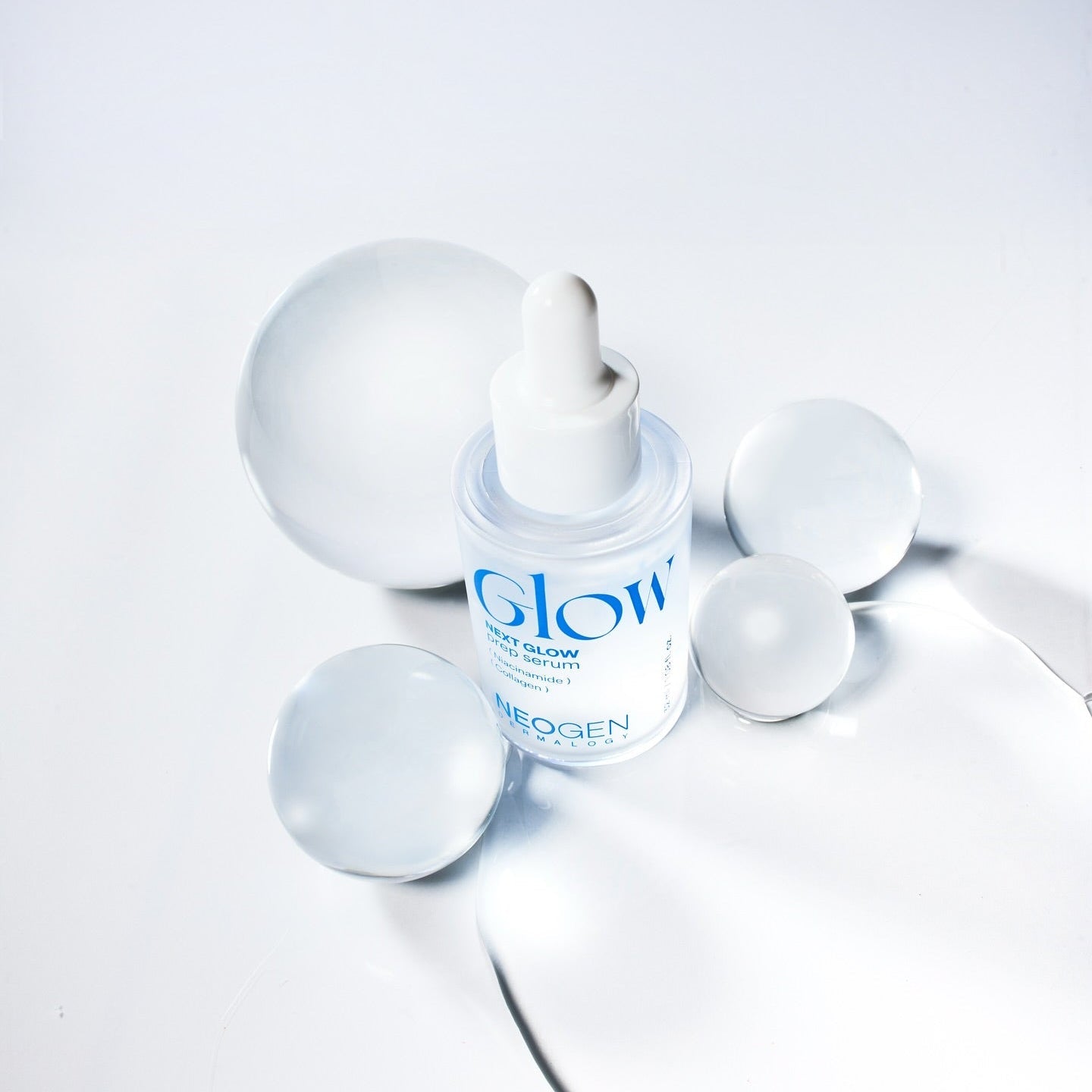 Bottle of NEOGEN Next Glow Prep Serum 32ml with surrounding spheres on a white background