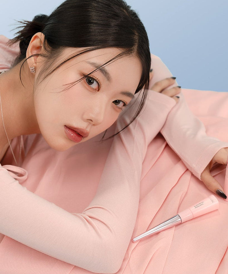 Woman posing with NEOGEN Slim Metal Mascara 6ml on a pink fabric background.