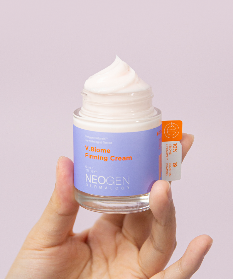 Person holding a jar of NEOGEN V Biome Firming Cream 60g with lid off, showcasing the product texture against a light background.