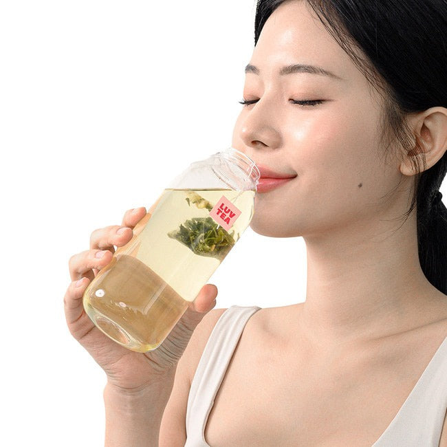 Woman enjoying NOTHING BETTER Luv Tea Lemon Green Tea (X15) from a clear bottle, showing a relaxing tea experience.