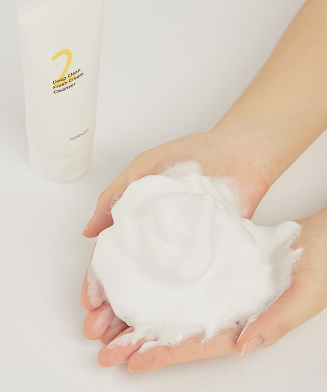 Foamy texture of NUMBUZIN No.2 Deep Clean Cream Cleansing Foam 120ml on hands next to product packaging.