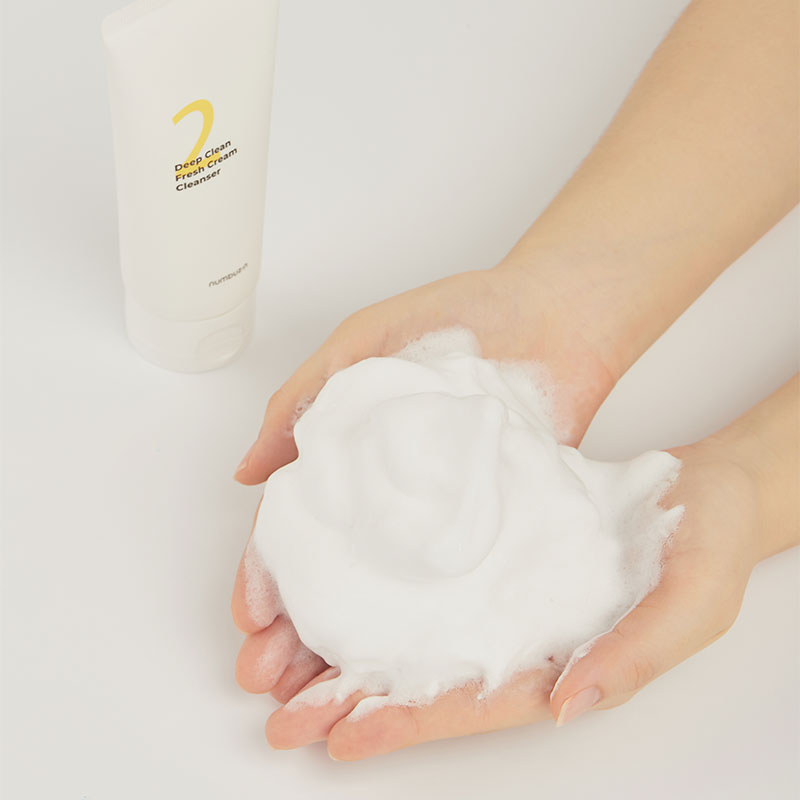 Foamy texture of NUMBUZIN No.2 Deep Clean Cream Cleansing Foam 120ml on hands next to product packaging.