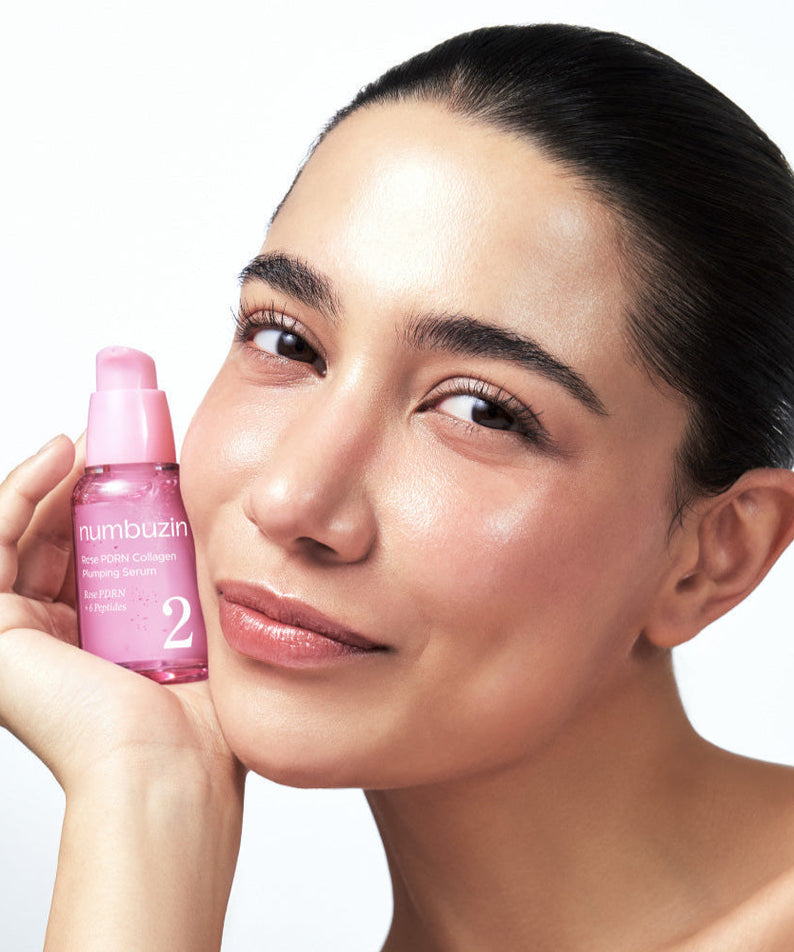 Smiling woman holding NUMBUZIN No.2 Rose PDRN Collagen Plumping Serum 30ml bottle next to her face.